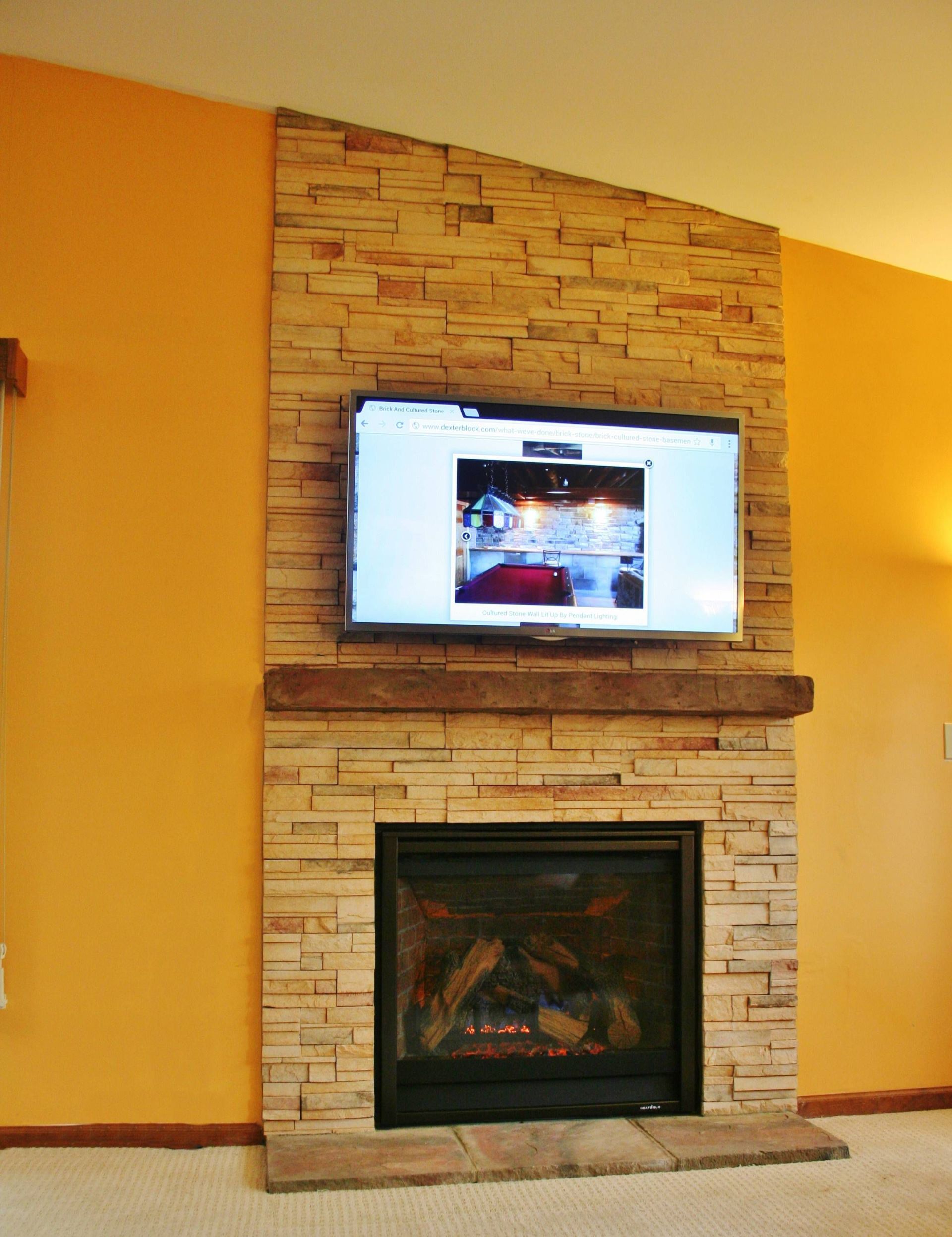 Living room fireplace with stone surround and a TV mounted above it on orange walls