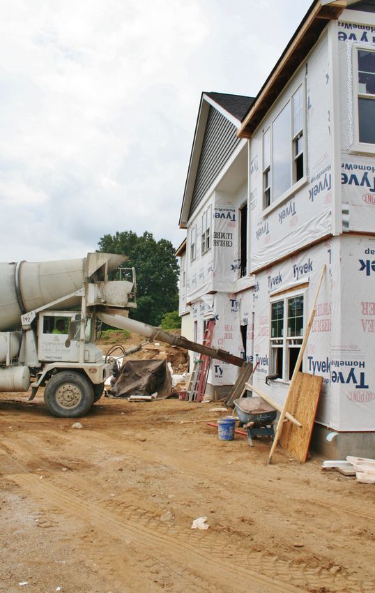 Cement truck pouring concrete beside a house under construction on a dirt road