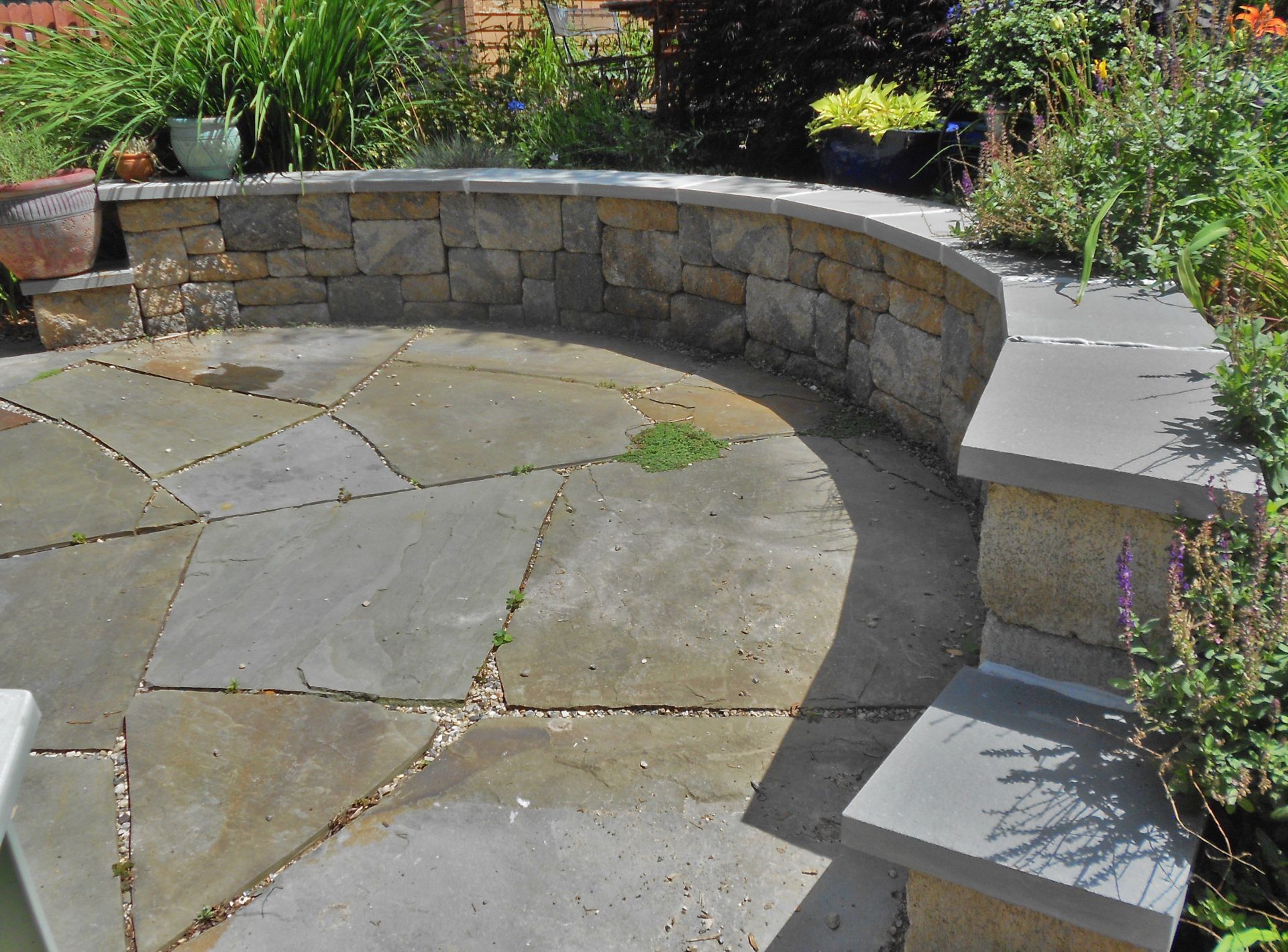 Curved stone patio bench beside a flagstone courtyard with garden plants