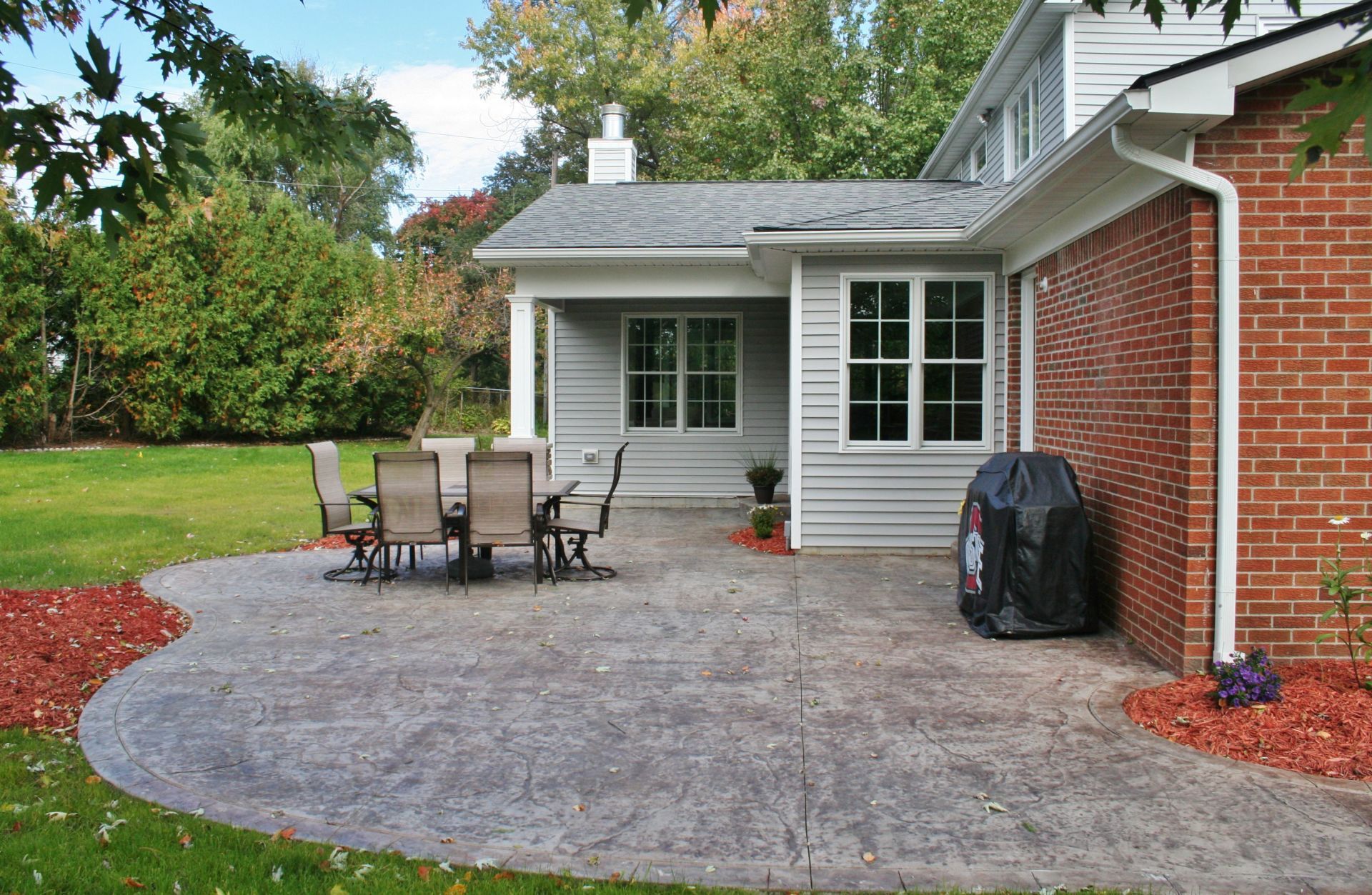 Backyard patio with outdoor dining set beside a white house and brick wall