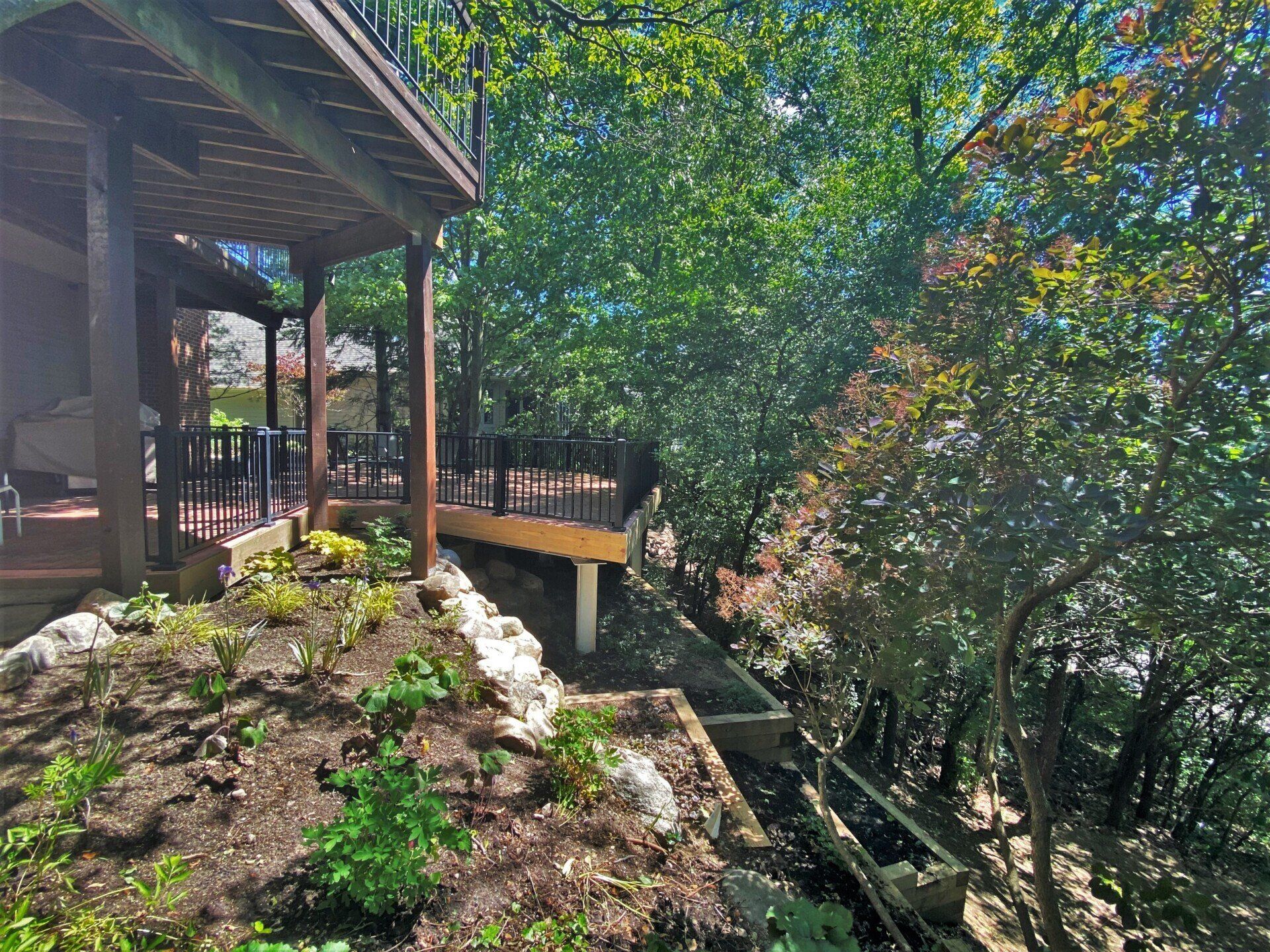 Wooden deck and railing beside a rocky garden path under leafy trees