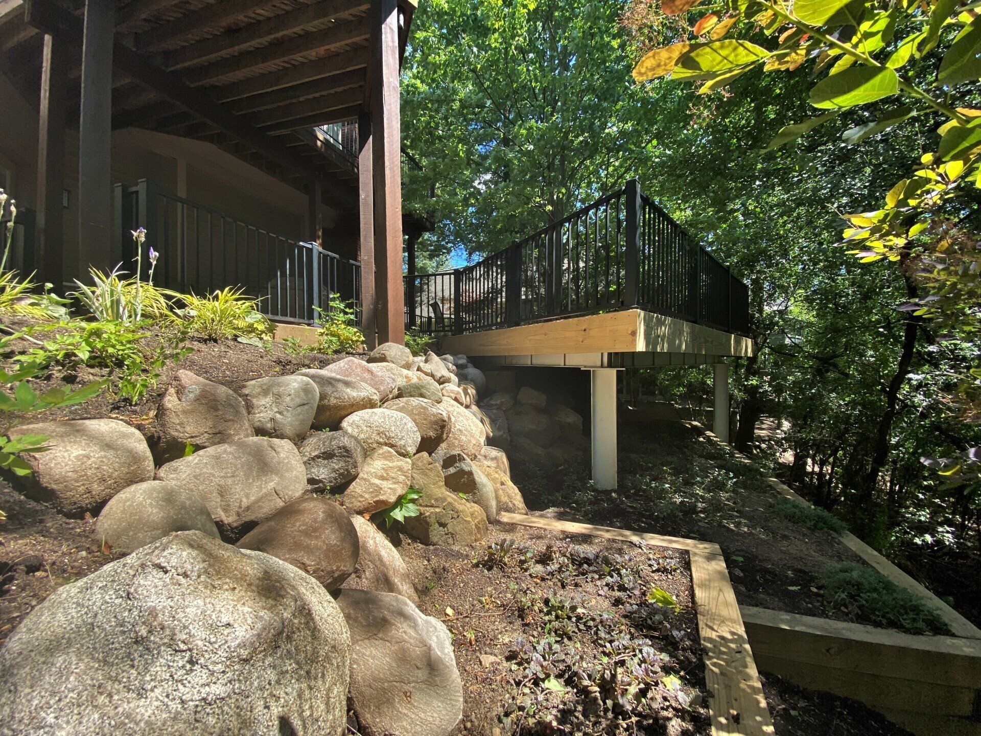 Rock retaining wall beside a house deck and ramp in a wooded yard