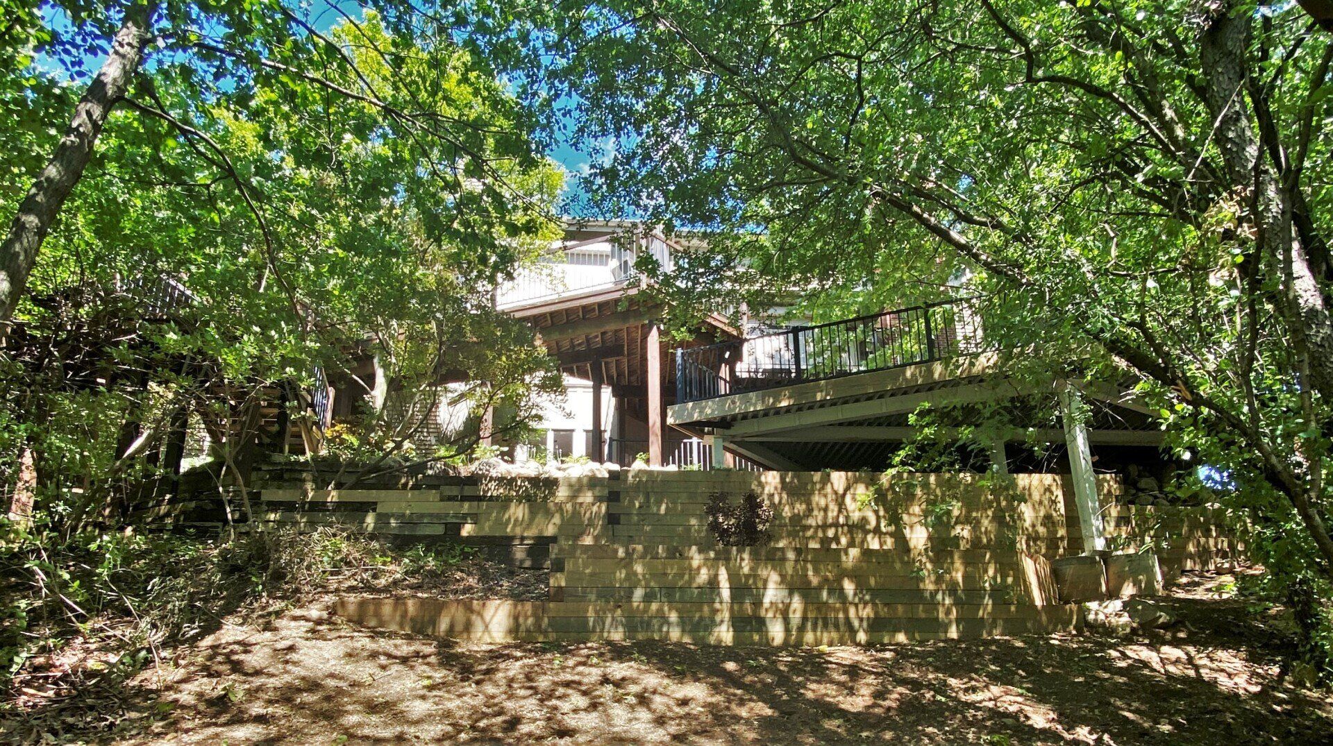 Tree-shaded historic house behind a low stone wall, with green foliage framing the scene.
