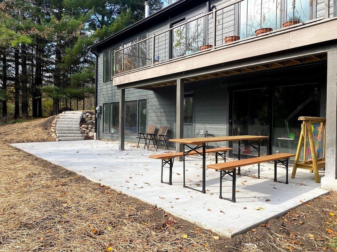 Modern house patio with wooden picnic tables and concrete terrace beside wooded hillside