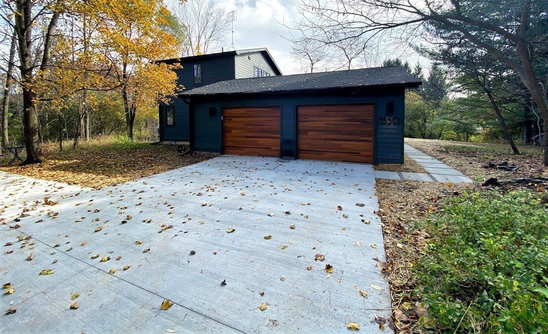 Modern house with double garage and a snow-dusted driveway surrounded by autumn trees
