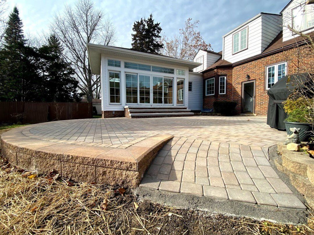 Backyard patio with brick paving, stone steps, and a white sunroom attached to a house