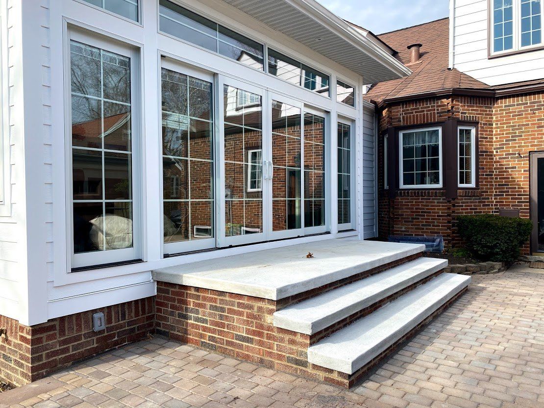 White house porch with large windows, brick steps, and a paved driveway