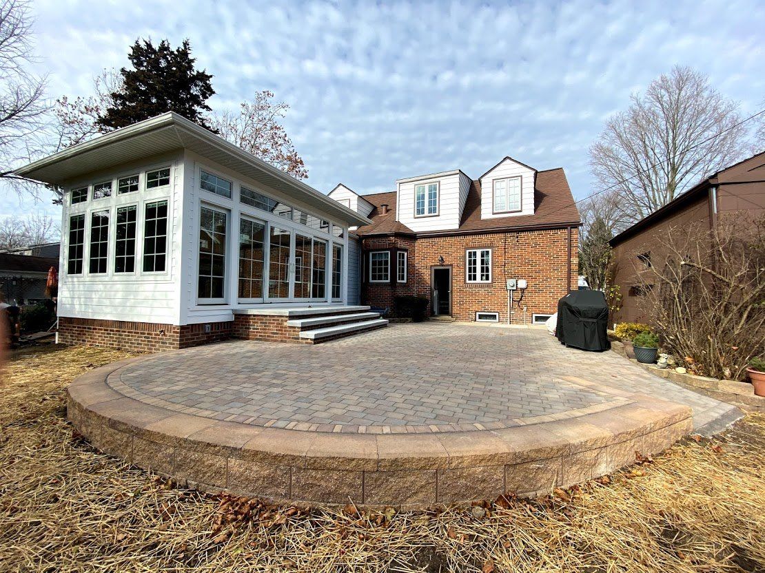 Brick house with white sunroom and circular stone patio in a backyard
