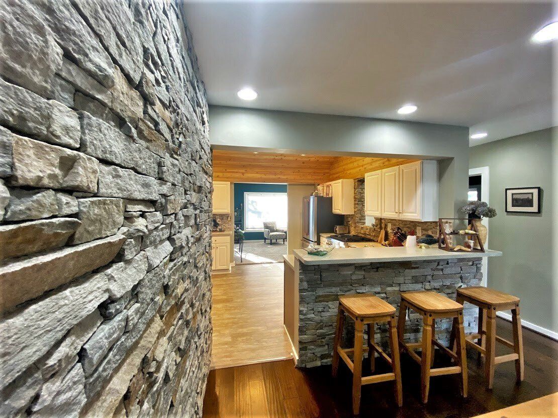Modern kitchen with stone accent wall, wooden island, and three stools in an open, warmly lit home interior