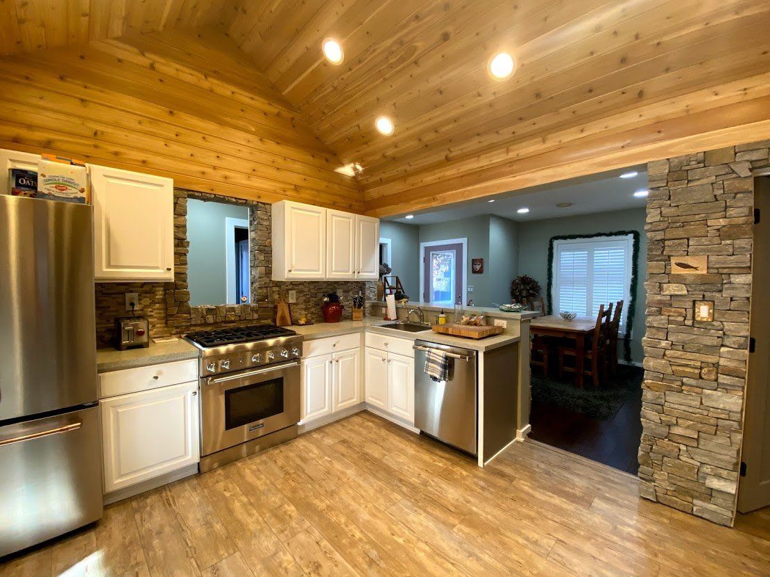 Wood-paneled kitchen with white cabinets, stainless fridge, stone column, and open view to dining area