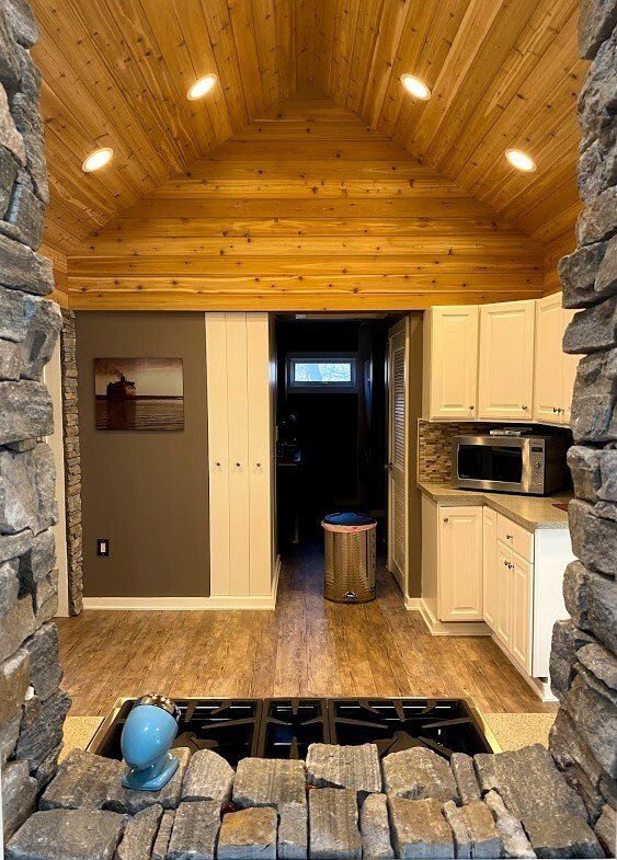 Cozy rustic kitchen with stone fireplace, wood vaulted ceiling, white cabinets, and tiled floor
