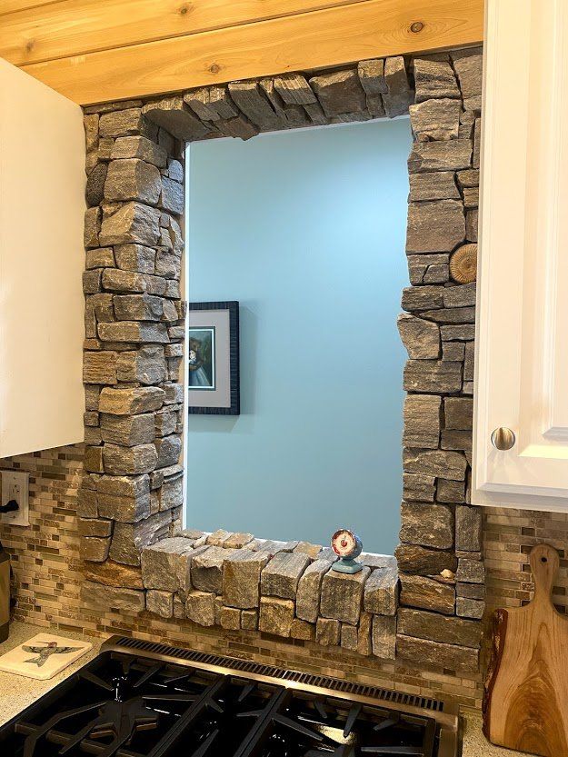 Stone-framed wall mirror above a kitchen stove, reflecting a blue room and framed art