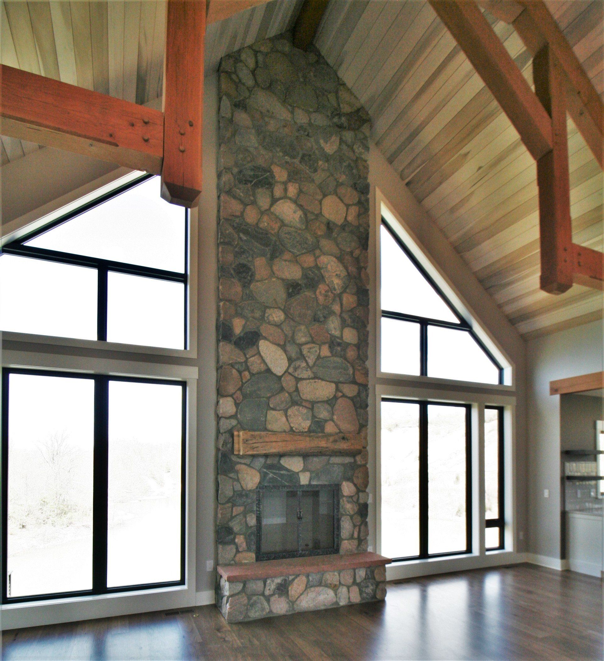 Great room with stone fireplace, vaulted wood ceiling, and large windows letting in bright daylight