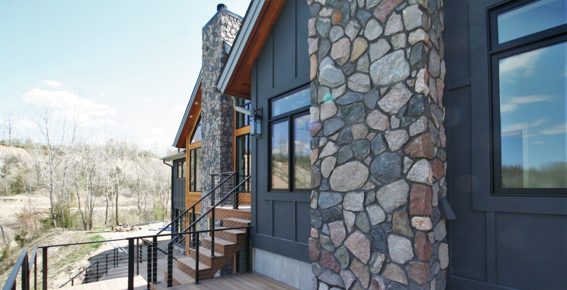 Stone-sided modern house with large windows and a small stairway on a hillside.