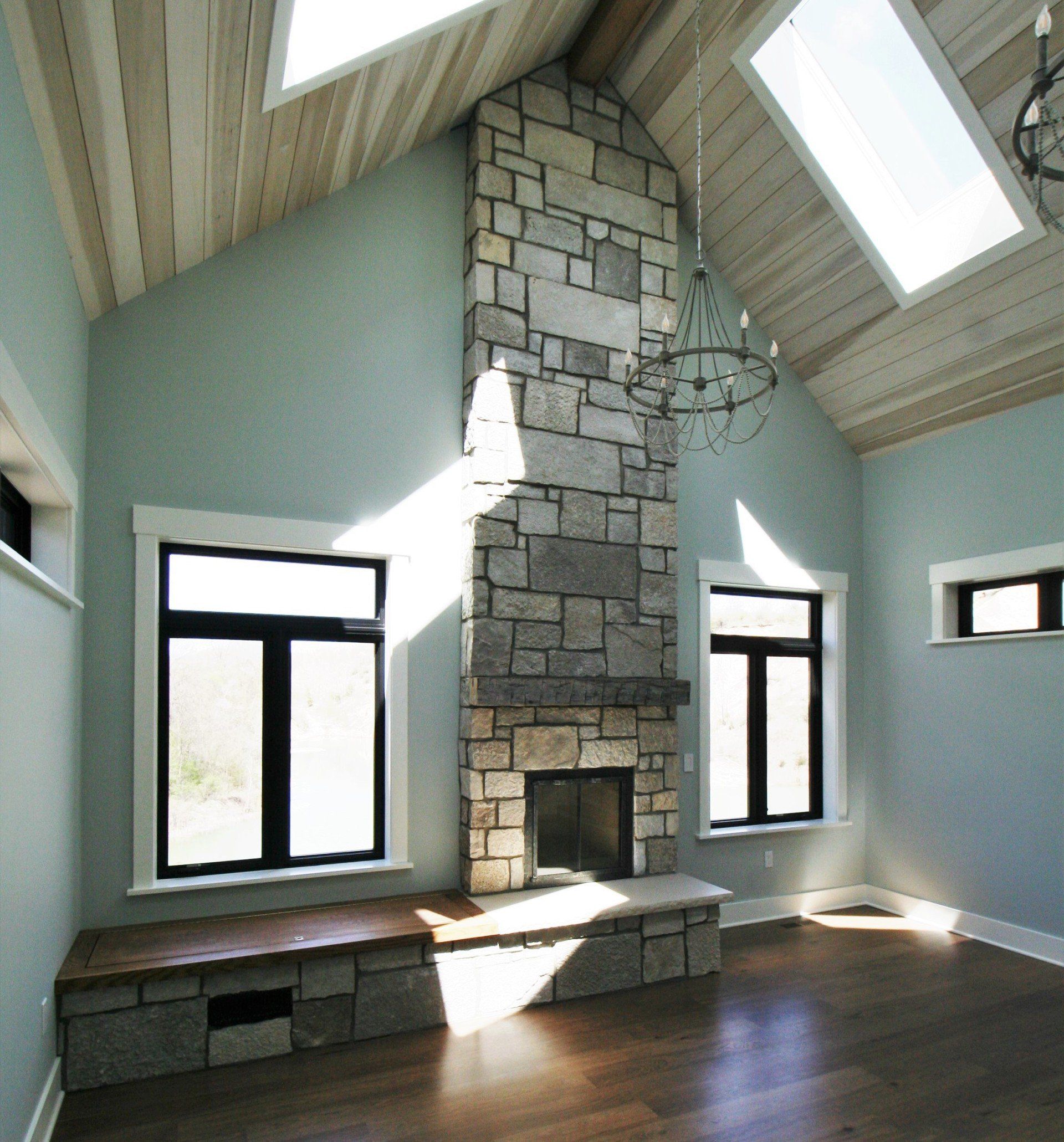 Bright living room with vaulted ceilings, skylights, and a stone fireplace centered between windows