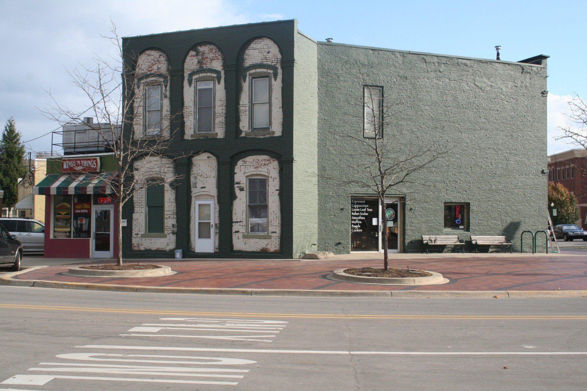 Corner building with faded green brick, black-painted facade, and storefronts on a city street.