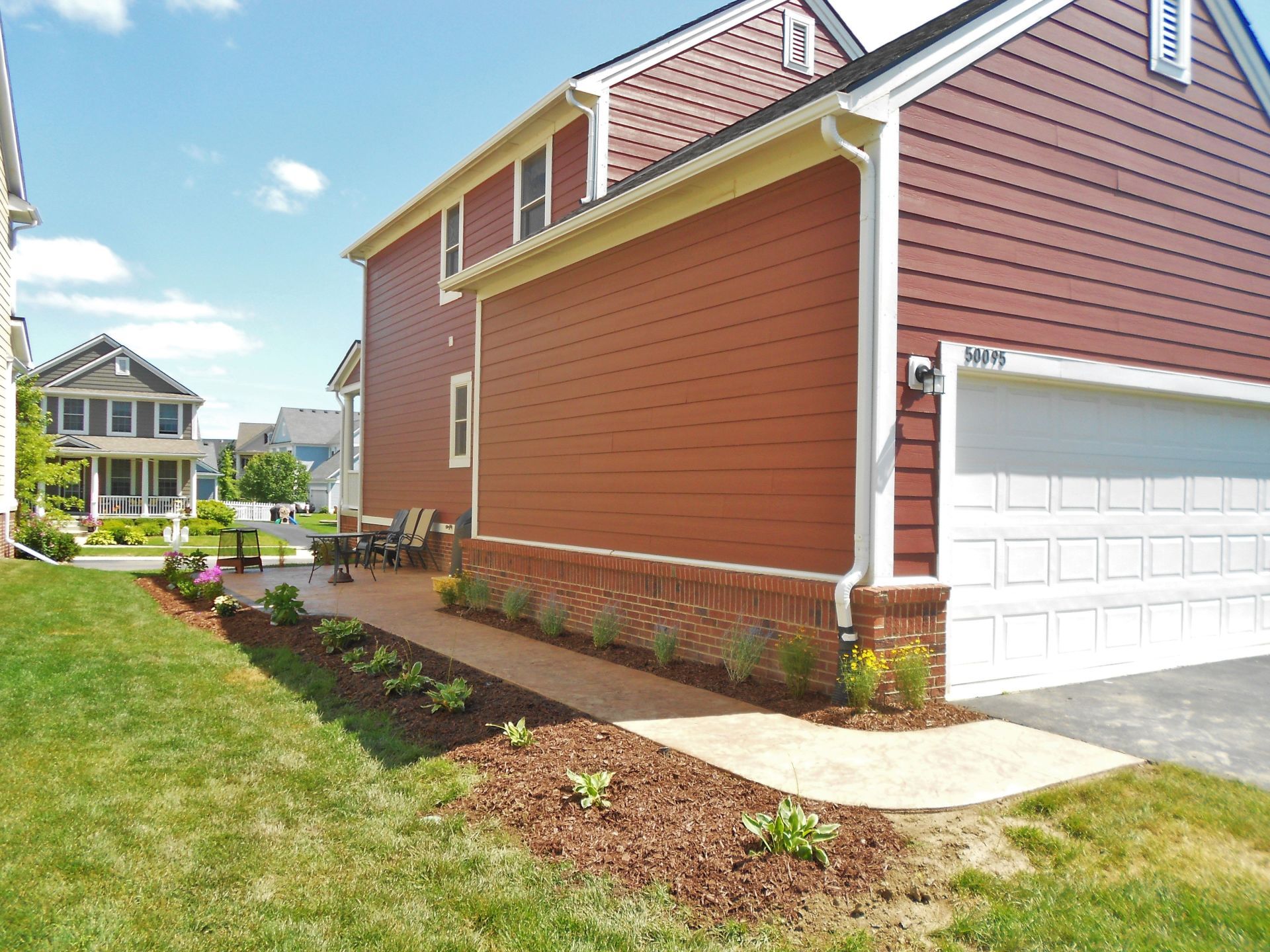 Suburban house exterior with red siding, white garage, and landscaped front yard under a blue sky