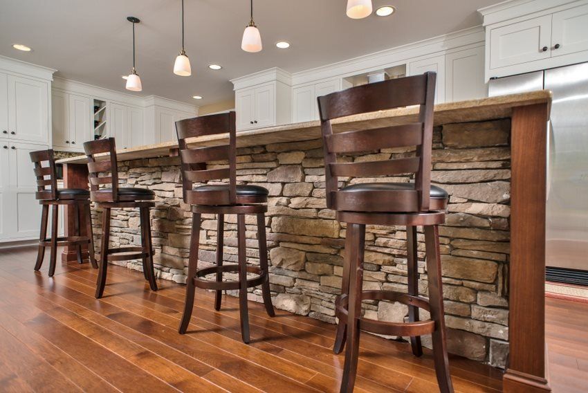 Modern kitchen island with stone facade, hardwood floors, and four dark wooden bar stools