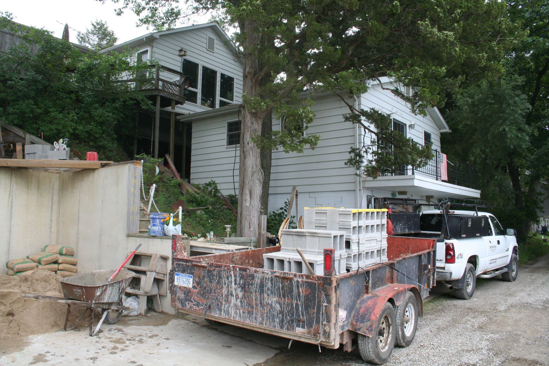 Old white house on a dirt lot with a rusty trailer and white pickup truck under trees