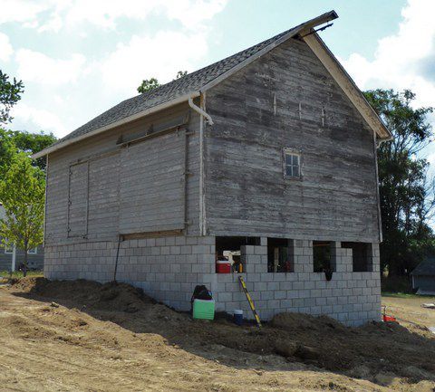 Unfinished wooden house with gray cinder block foundation on a dirt lot.