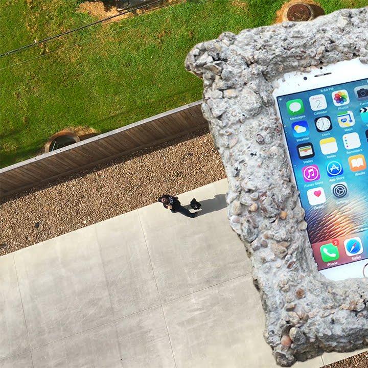 Aerial view of a person standing by a giant smartphone-shaped rock on a driveway.