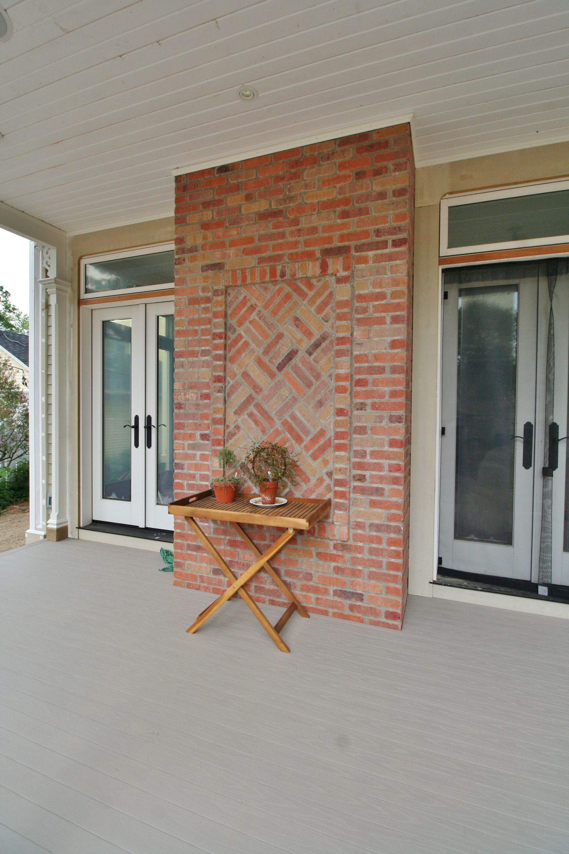 Brick porch wall with a small folding table and potted plants between two glass doors