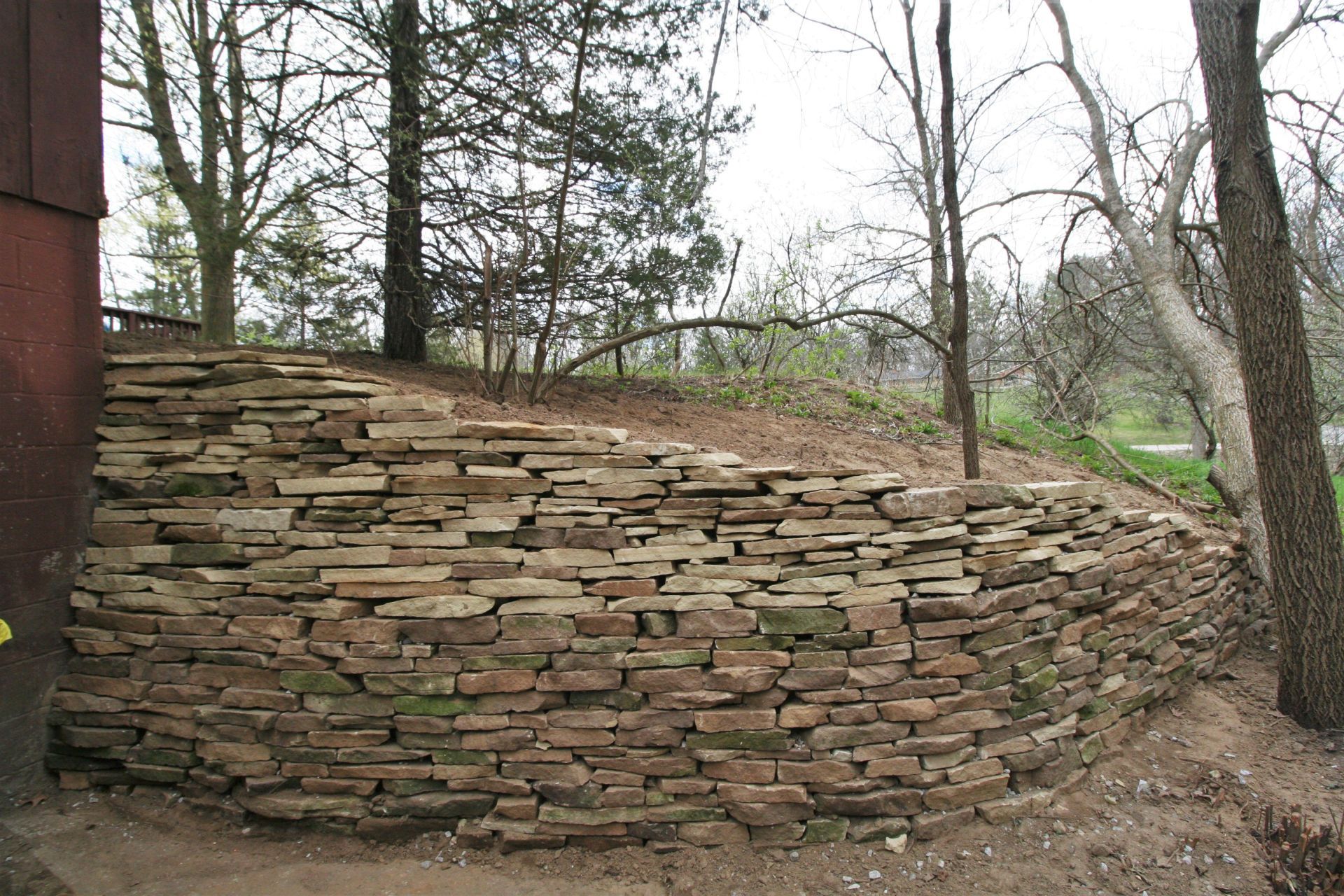 Curved dry-stack stone retaining wall holding back a wooded hillside