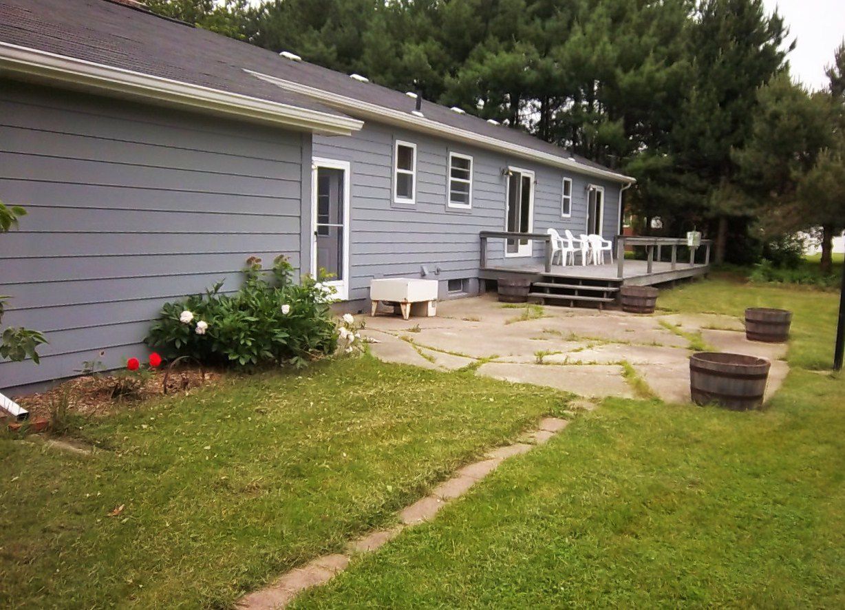 Gray house with a grassy yard, stone path, and a small deck with steps and potted plants.
