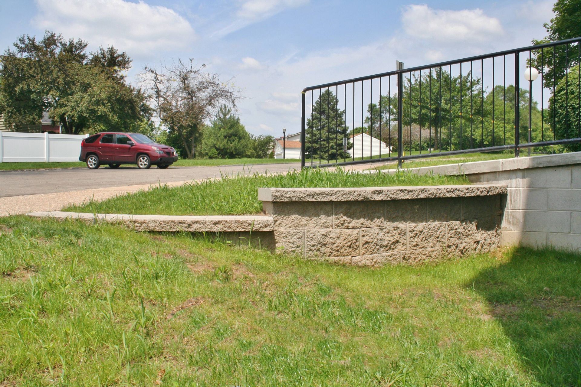 Grassy roadside embankment with a red van, stone wall, and black metal fence under a cloudy sky