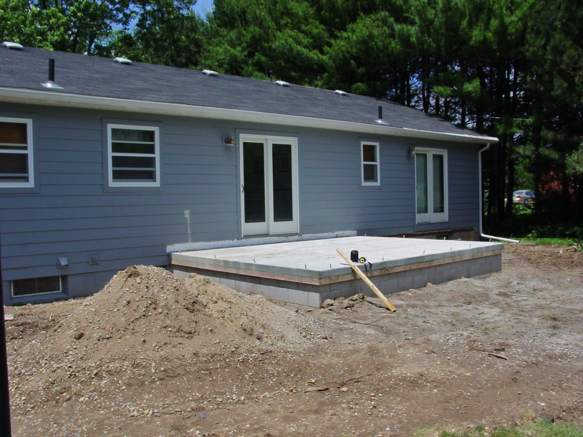 Backyard deck under construction beside a gray house, with a dirt mound and tools nearby