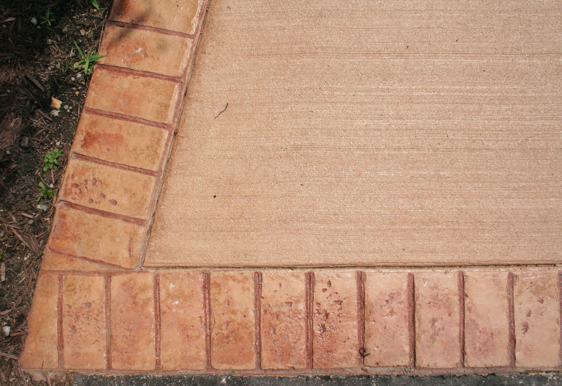 Brick-bordered concrete walkway corner with adjacent soil and plants
