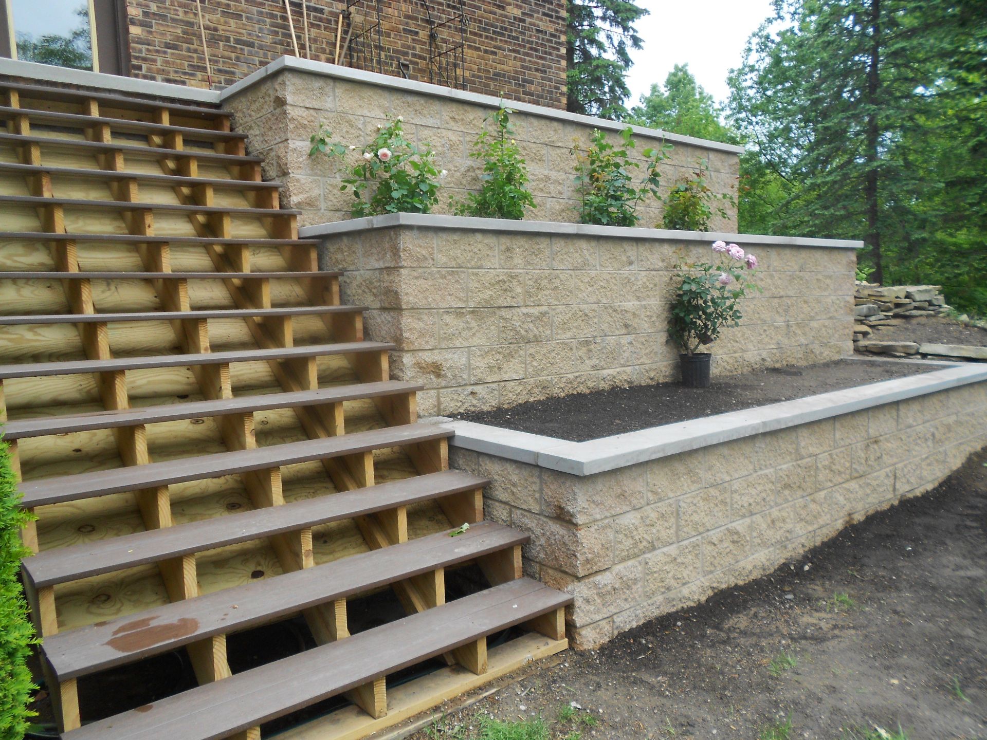 Wooden outdoor staircase beside stone retaining walls and a landscaped terrace in a garden setting