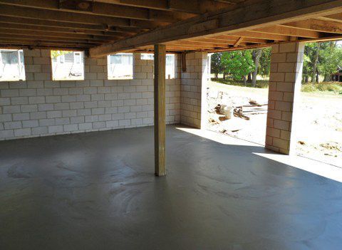 Empty concrete room with unfinished block walls, exposed ceiling beams, and open window and doorway openings.