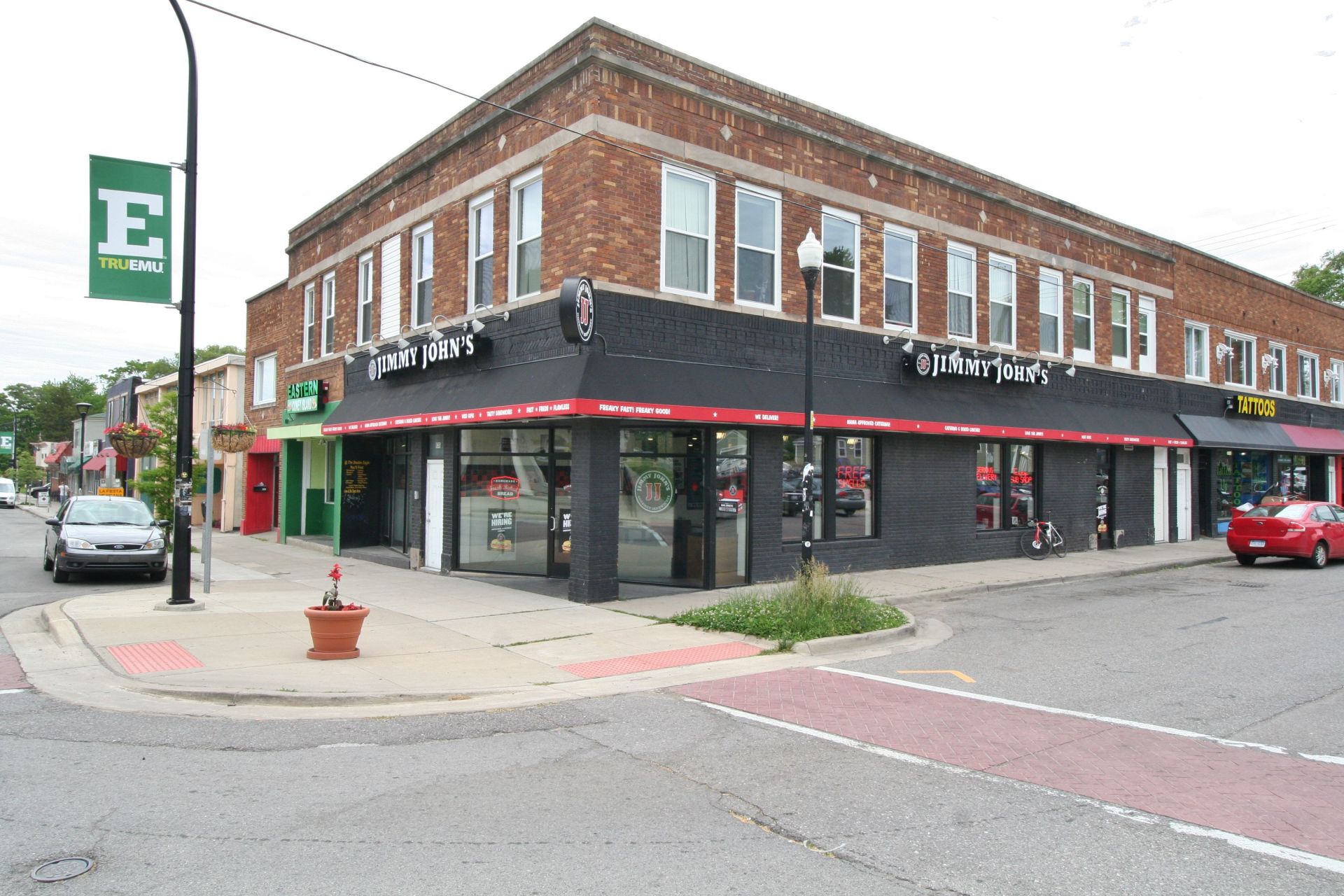 Corner storefronts in a brick building with black awnings on a city street corner