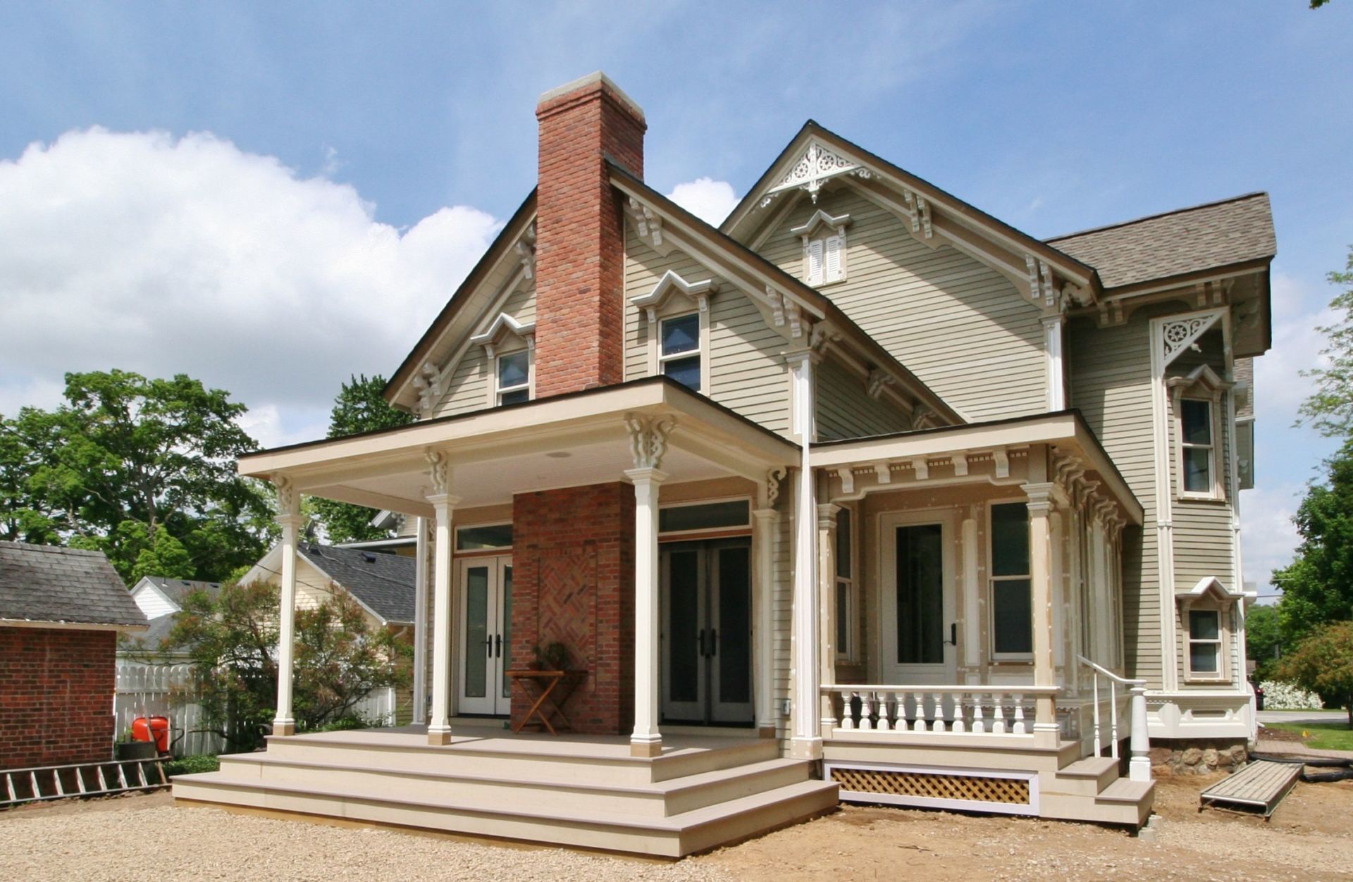 Victorian-style house with a porch, brick chimney, and white trim under a partly cloudy sky