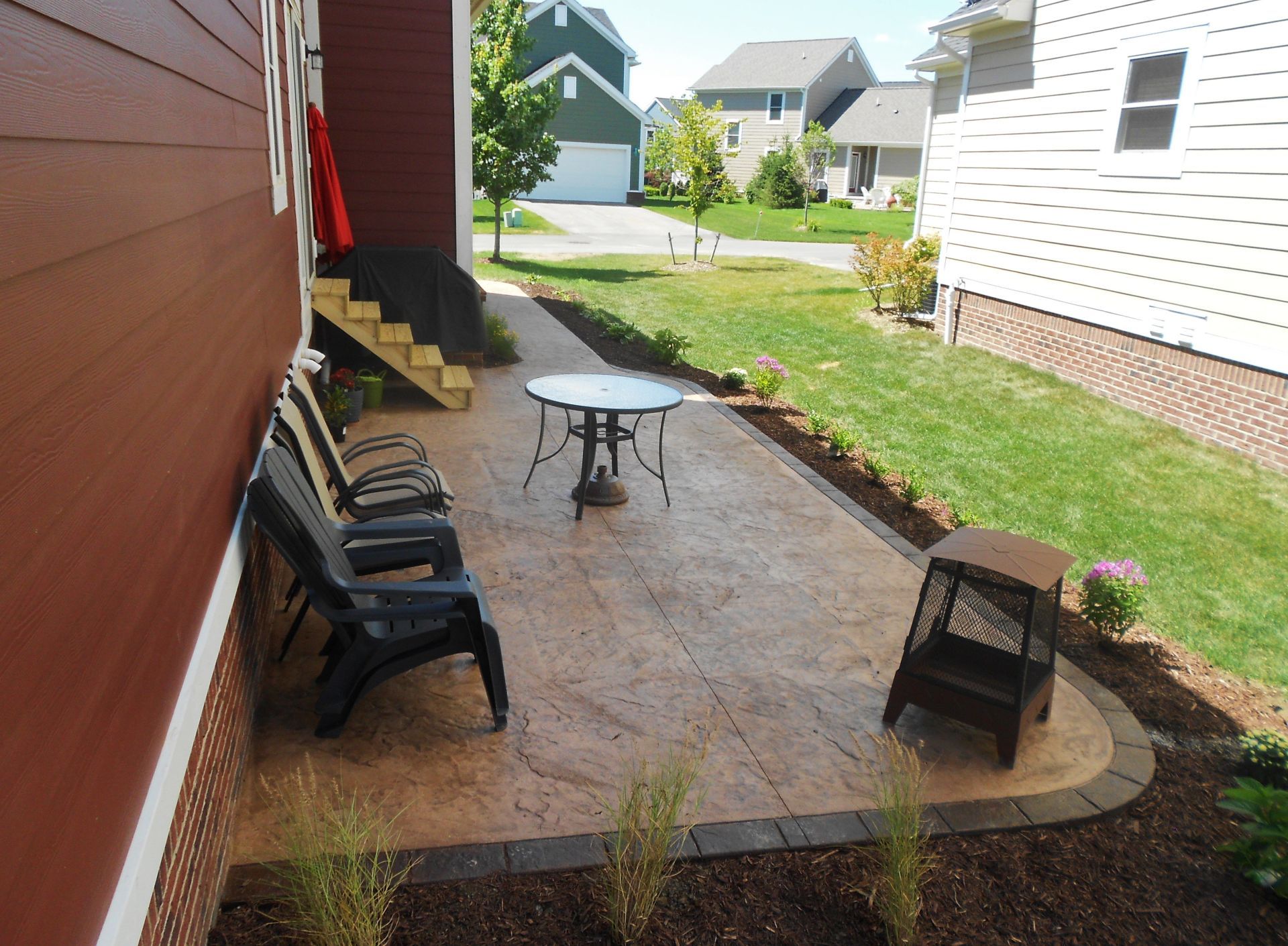 Back patio with chairs and a table beside a red house and white siding, overlooking a grassy yard