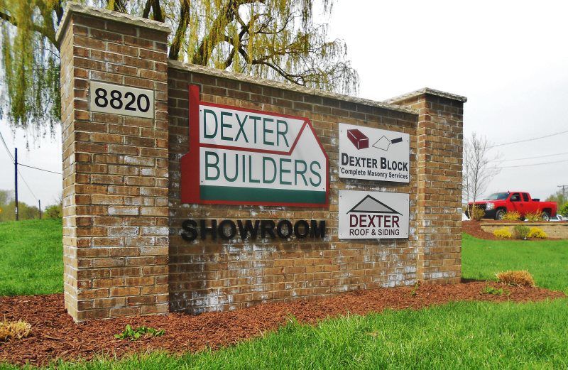 Dexter Builders showroom sign on a brick pillar by a grassy roadside, with address 8820.
