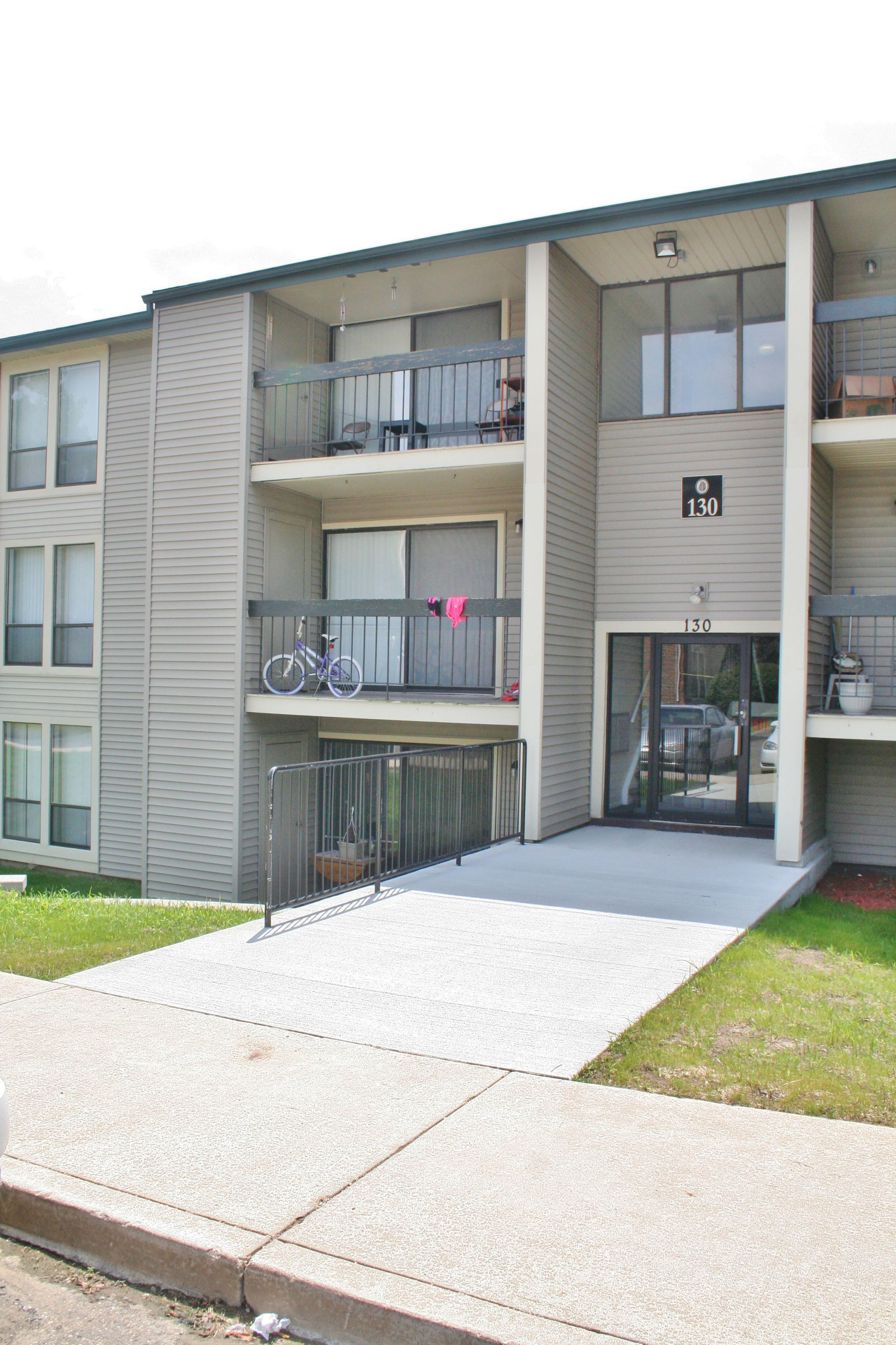Apartment building entrance with ramp and balconies, viewed from the sidewalk