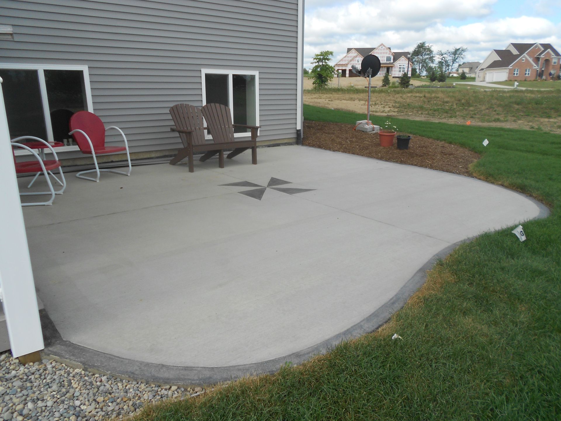 Concrete patio beside gray house with chairs, star inlay, and grassy yard.