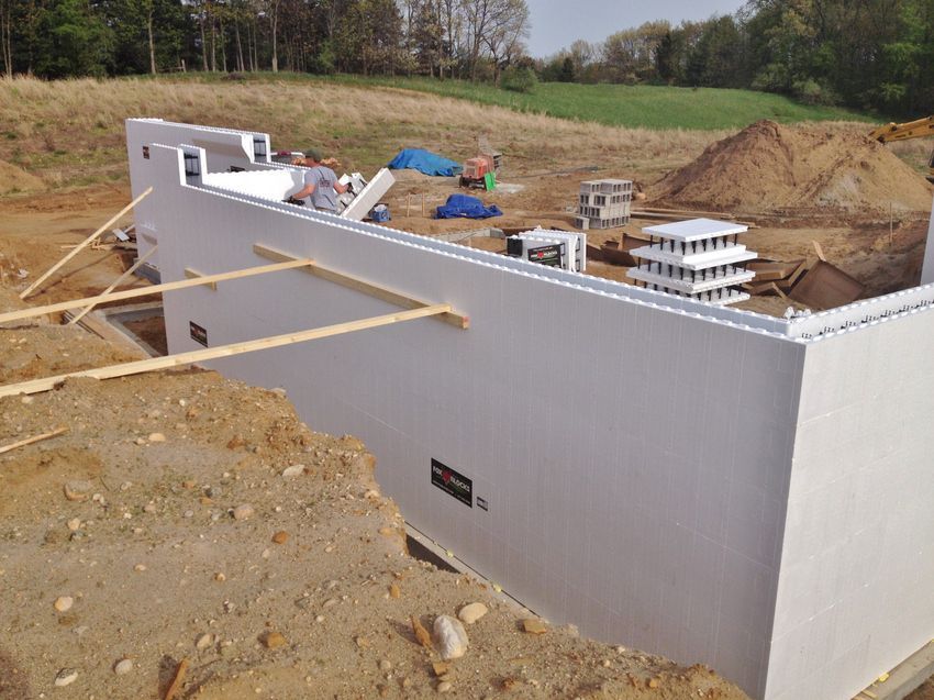 Partially built concrete foundation wall at a construction site with materials and dirt around it