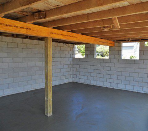 Unfinished basement with cinder block walls, exposed wooden beams, and a concrete floor.