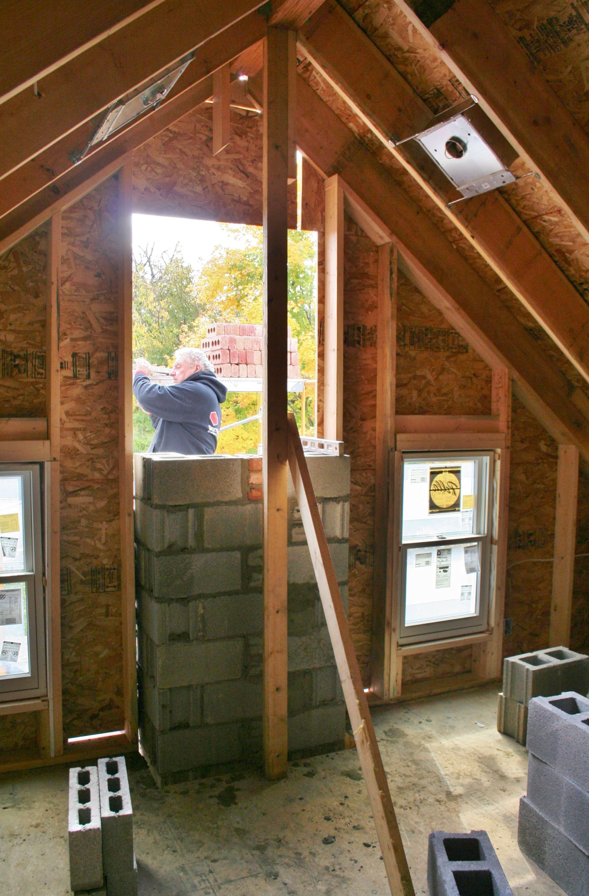 Unfinished attic with exposed rafters and a person seen through a window opening stacking cinder blocks
