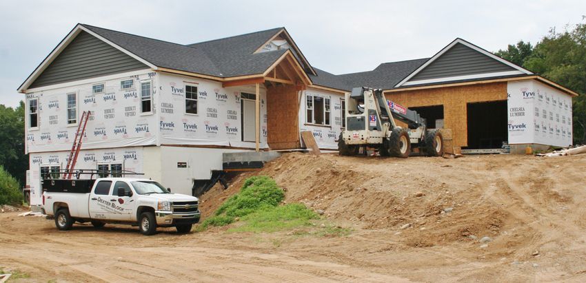 New home under construction with white truck parked on a dirt lot and a garage beside it