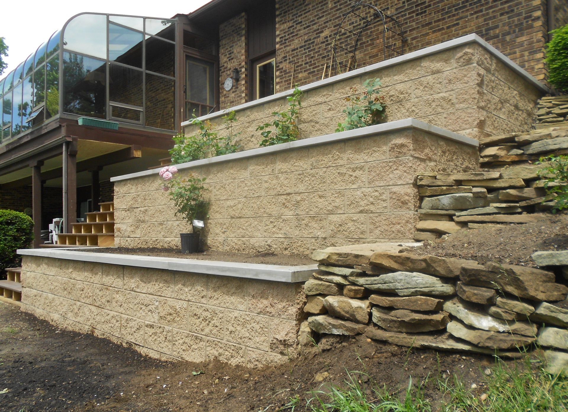Terraced stone retaining walls beside a house with a covered deck and stone steps