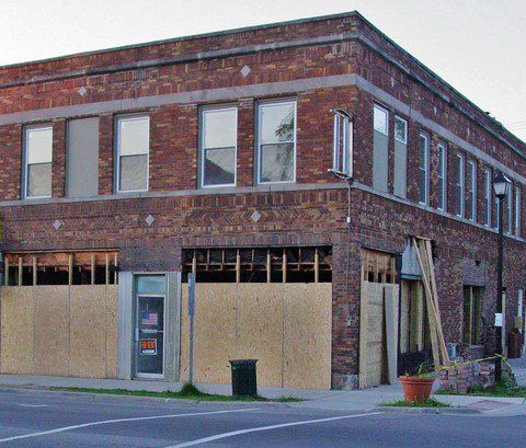 Boarded-up brick corner building with broken windows and a closed storefront on a street corner