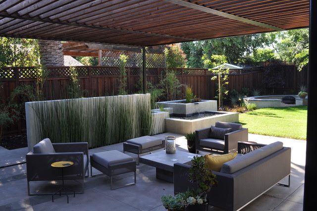 Modern patio with dark lounge furniture, striped privacy screen, and covered pergola in a landscaped backyard