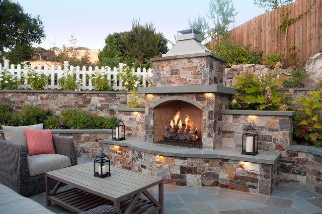 Stone outdoor fireplace with seating on a patio at dusk