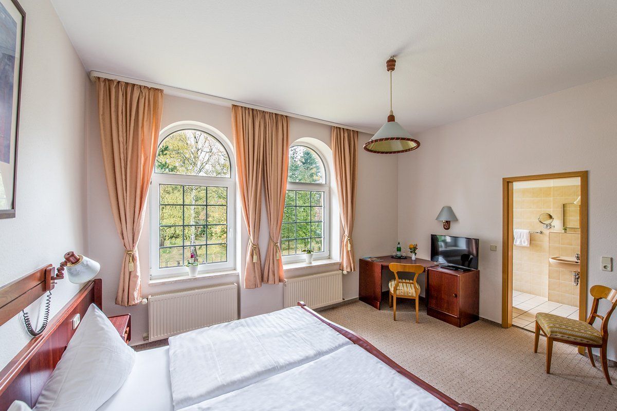 Ein Hotelzimmer mit einem Bett, einem Schreibtisch, einem Stuhl und zwei Fenstern.