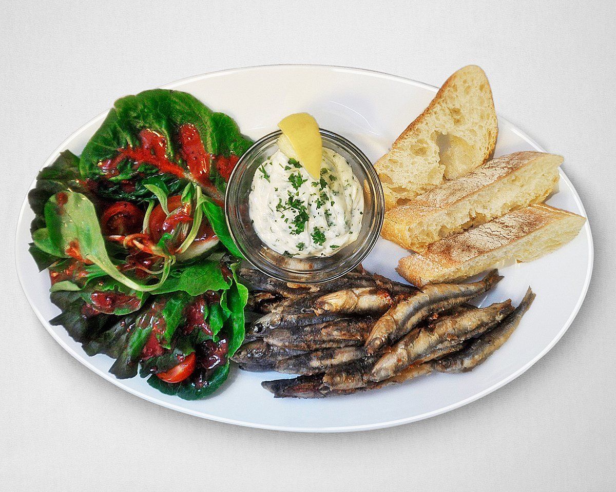 Ein weißer Teller mit Fischbrot und Salat