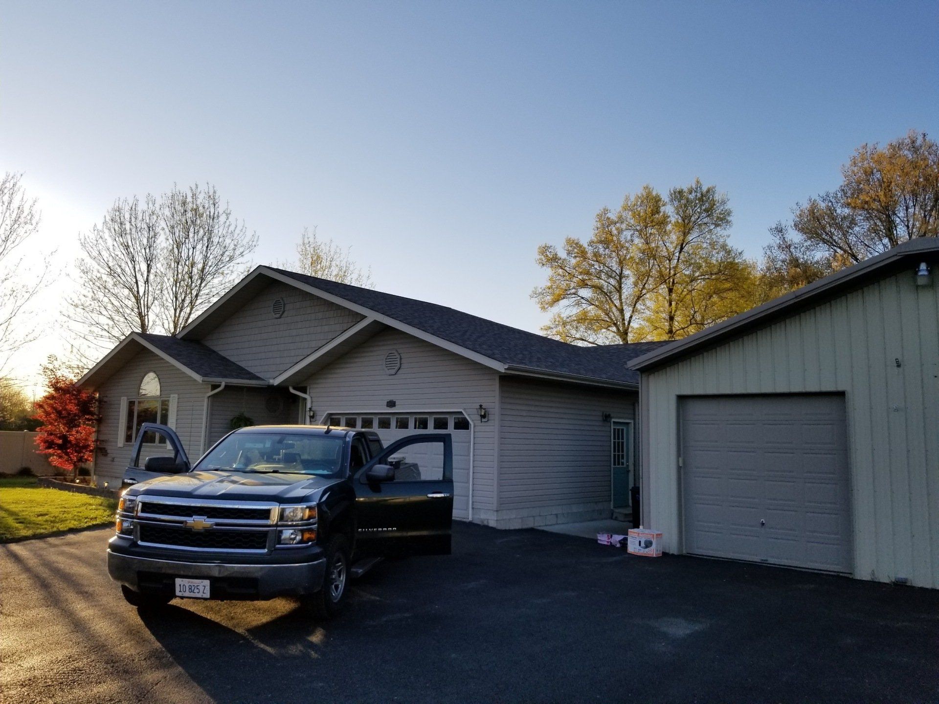 A dark-colored pickup truck with its driver-side door open is parked in the driveway of a light-colored suburban home.